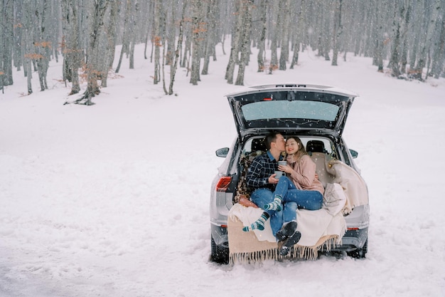 雪の降る車のトランクに抱きしめて座っている間ガイは女を寺院でキスします