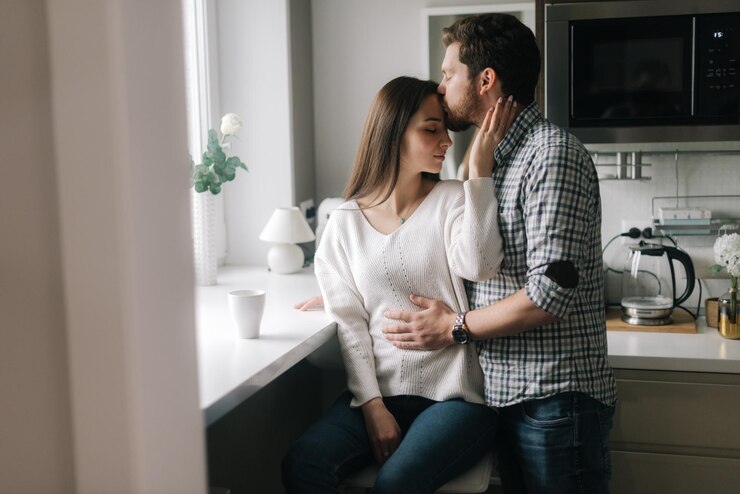 Photo guy kisses his girlfriend on the forehead in th kitchen by the window. daily life of a male and female in apartment.