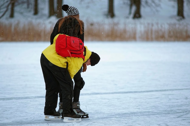 Парень учит девушку кататься на коньках на замерзшем озере зимой Тракай. Катание на коньках включает в себя любую деятельность, которая заключается в перемещении по льду на коньках.
