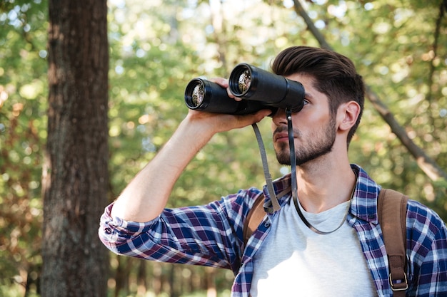 Guy looking at binoculars in forest