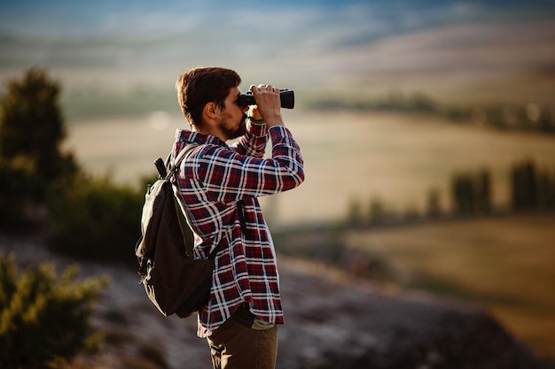 Guy looking at binoculars in hill man in tshirt with backpack