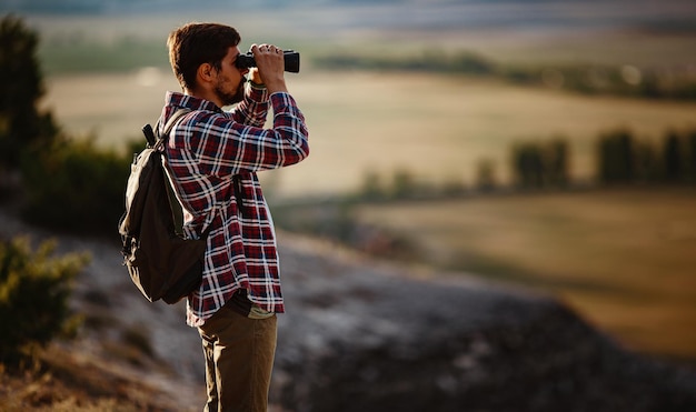 Guy looking at binoculars in hill man in tshirt with\
backpack