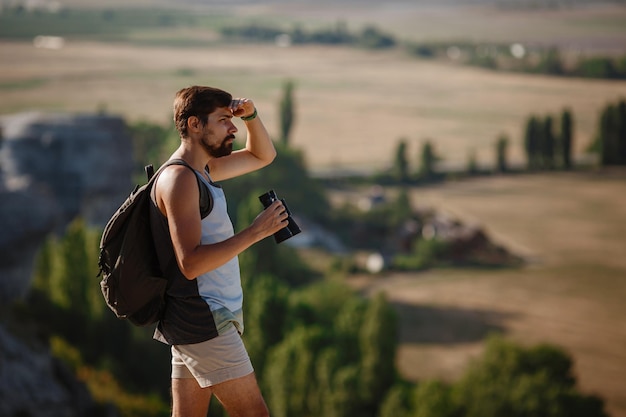 Guy looking at binoculars in hill man in tshirt with backpack