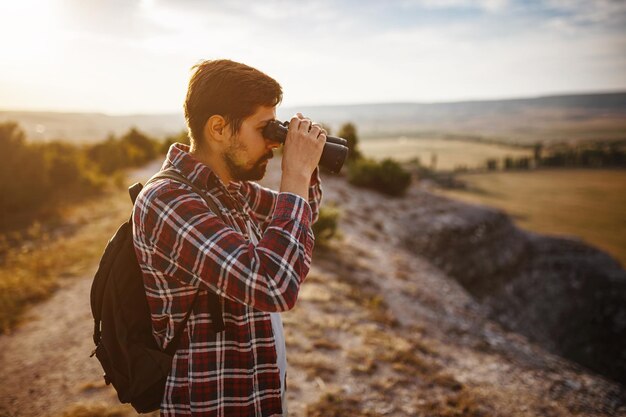 Guy looking at binoculars in hill man in tshirt with\
backpack