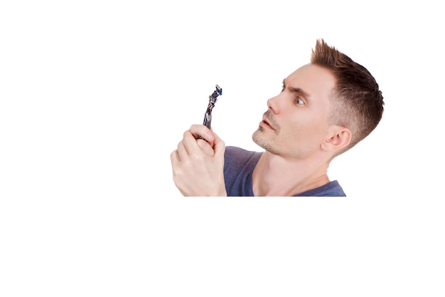 The guy looks scared at the razor. Young guy shaves his face with a razor on a white background. Handsome men are shave and beard. Copy Space.