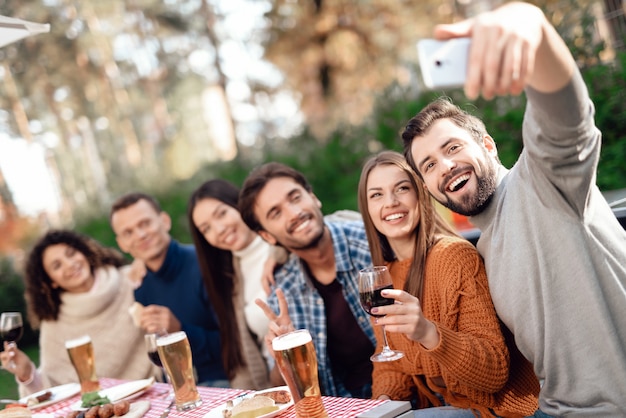 The guy makes selfie with friends on the smartphone.