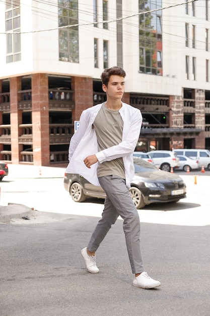 Guy model met een stijlvol kapsel poseren buiten in een wit overhemd en grijze broek. trendy kapsel ligt in de buurt van een modern zakencentrum. Aantrekkelijke man in de straat op een zomerdag.