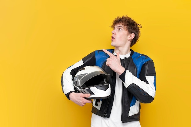 guy motorcyclist in leather jacket holds helmet and points to the copy space on yellow background