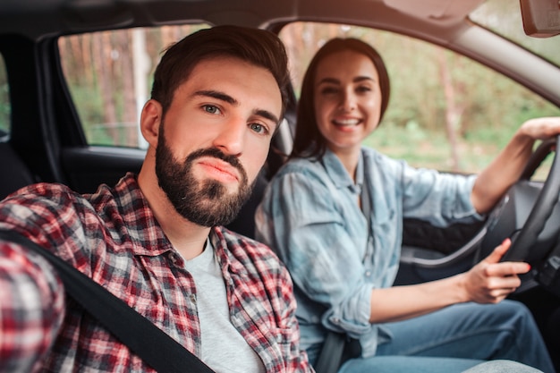 Guy neemt selfie in de auto met zijn vriendin. Ze kijkt op de camera en lacht. Het meisje houdt haar handen op roer.