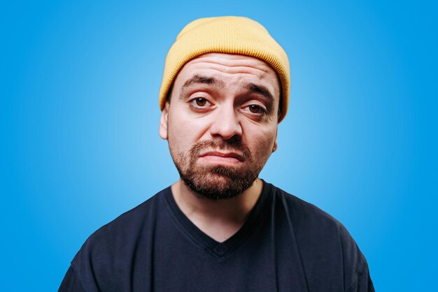 A guy photo of a tired exhausted and unhealthy looking man with an unhappy expression in a studio shot a blue background looking at camera face gaunt indicating a sense of depression and sadness