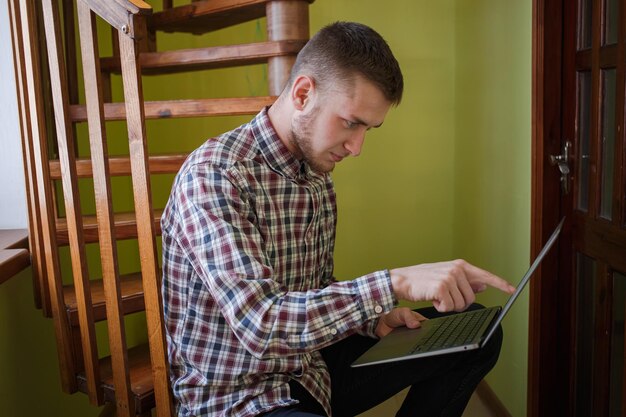 A guy in a plaid shirt looks at a laptop screen and points with his finger