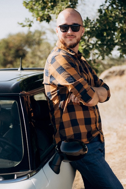 Guy in a plaid shirt next to a white car in nature