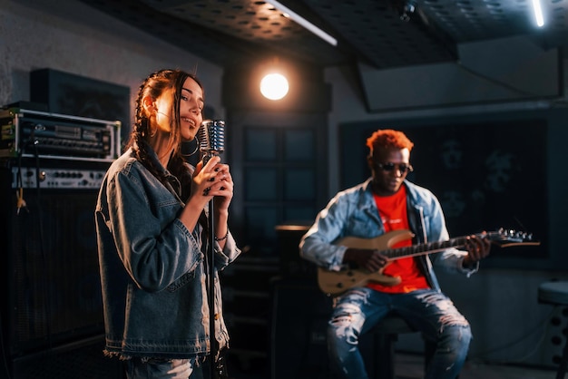 男はギターを弾く女の子は一緒にスタジオでリハーサルをしている白人の女の子とアフリカ系アメリカ人の男を歌う