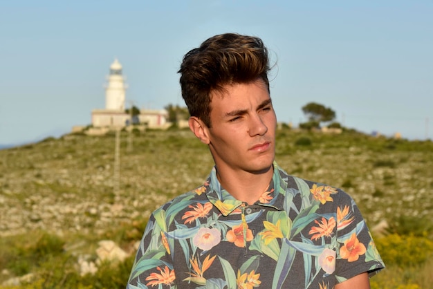 Guy poseert alleen op het strand, omringd door mediterrane vegetatie in de buurt van een vuurtoren