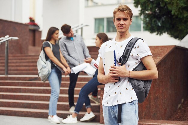 Guy posing for the camera. Group of young students in casual clothes near university at daytime.