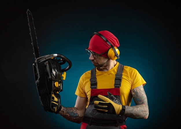 The guy in protective overalls with a chainsaw on a dark background