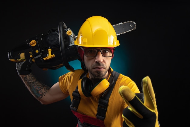 The guy in protective overalls with a chainsaw on a dark background