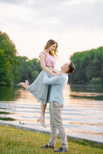 The guy raised his hands around the waist of his girlfriend up, looking at her, they smile and happy 