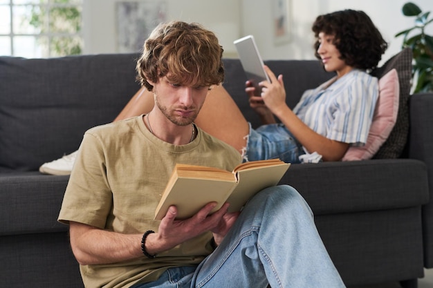 Guy reading novel with captivating subject against young woman with tablet