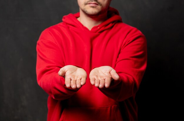 Photo guy in red sweatshirt show free hands gesture on dark wall