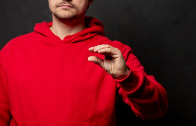 Guy in red sweatshirt show small gesture on dark wall