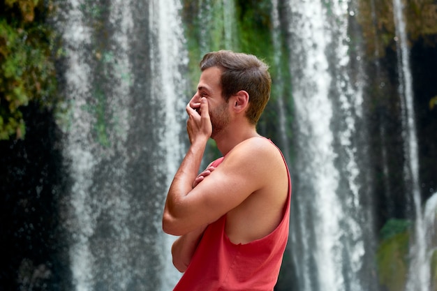 Guy in a red t-shirt laughing with a waterfall behind