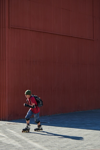 Guy rijdt op rolschaatsen op de stoep tegen de rode muur