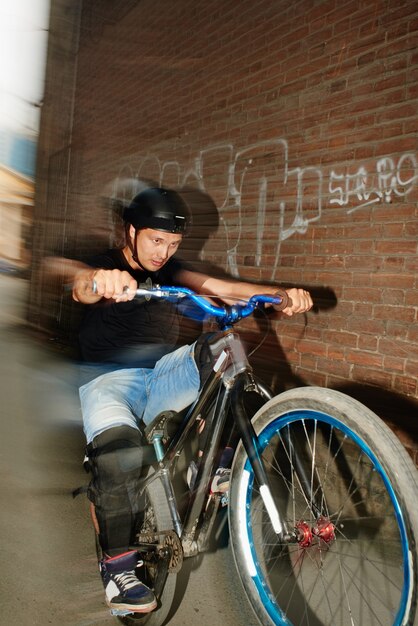 男は、赤レンガの建物の壁の近くで自転車の後輪に乗って動いているサイクリストです