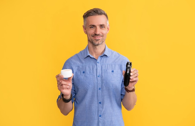 Guy showing electriv shaver and cream on yellow background personal care