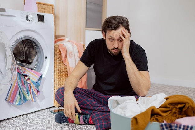 Guy sits on the laundry room floor with the washing machine\
open throwing all the clothes