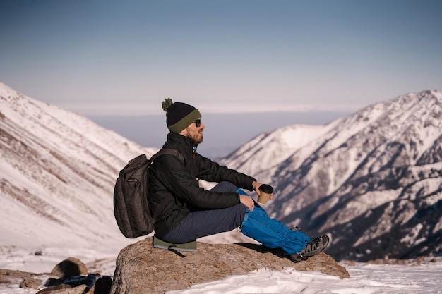 The guy sits on a stone against the backdrop of snowy mountains