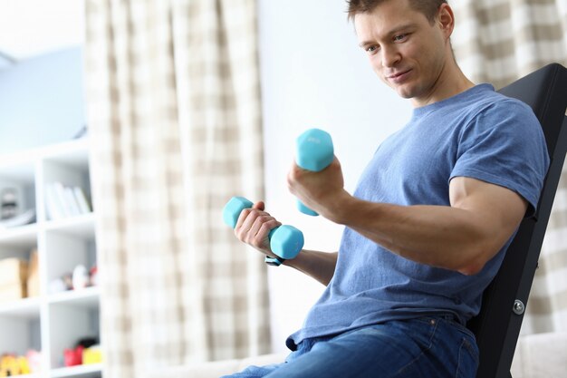 Guy sitting home simulator and looking dumbbells