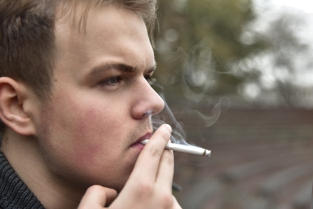 Guy fuma una sigaretta fuori, ritratto, da vicino