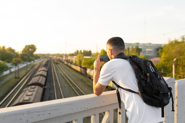 парень стоит на мосту фотографирует железнодорожные пути