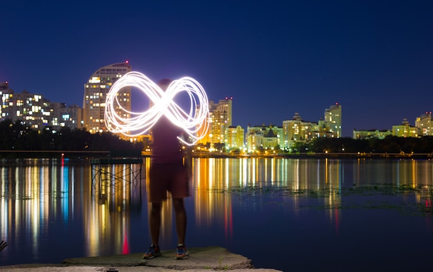 A guy stands on the banks of the Dnieper river against the background of a bright night embankment