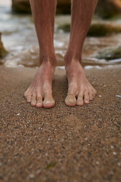 The guy stands on the sand barefoot Legs close up Sea Ocean