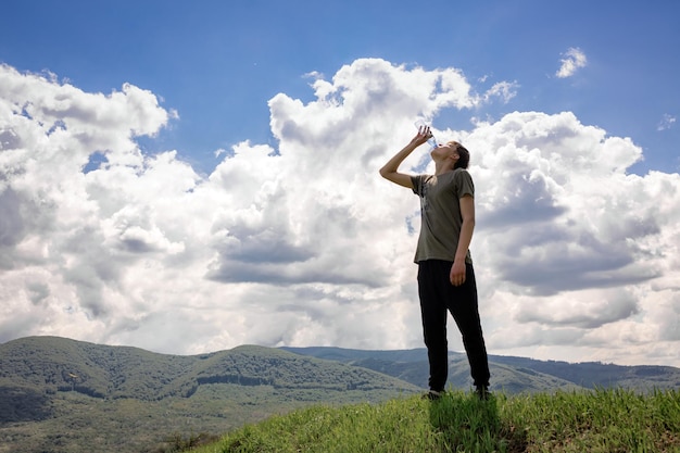 The guy stands on the top of the mountain and drinks water from a bottle Pure water