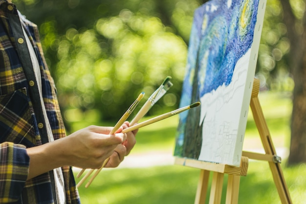 guy in a straw hat sits in the park in front of an easel