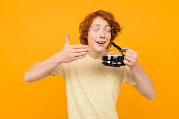 Guy student in een shirt drinkt koffie in een glazen mok op een gele muur
