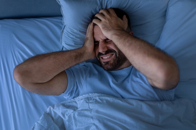 写真 頭痛に苦しむ男が寝室で夜に気分が悪くなる