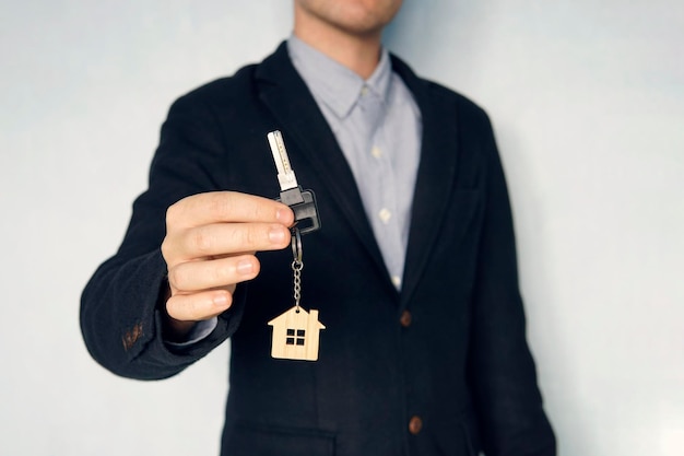 Guy in the suit shows me the keys Key chain in the form of a house in a man hand Holding house keys on house shaped keychain concept for buying a new home