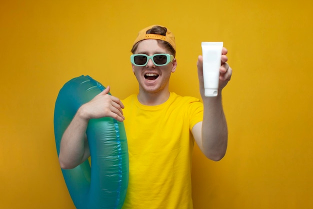 Guy in summer clothes and glasses on vacation holds a sunblock cream on a yellow background