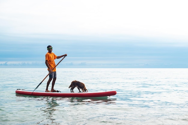 A guy on a sup board with a paddle with a dog stands on the sea in summer