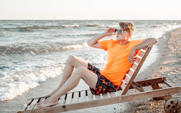 A guy in a T-shirt and shorts sits on a sun lounger by the sea