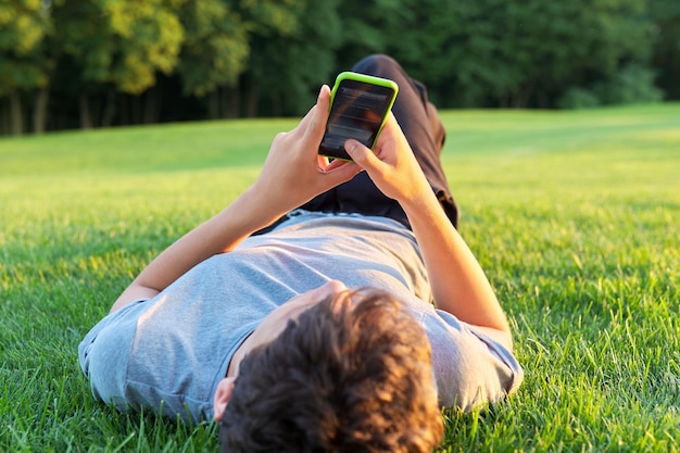 Guy teenager lying on grass with smartphone