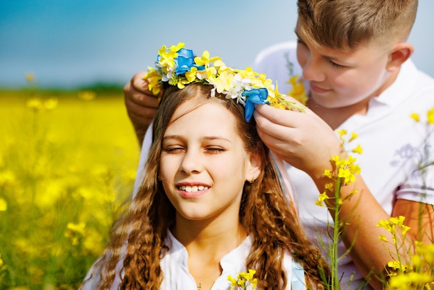Guy throws up ribbons in Ukrainian wreath on at his sister on her head against sky and fields