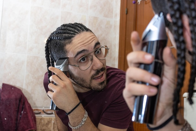 Guy in towel cutting his hair in front of mirror at home Health Care Concept