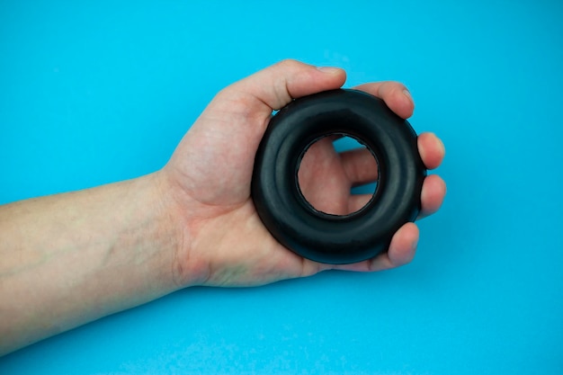 A guy trains his arms by squeezing a rubber expander to strengthen his arms on a blue background the concept of strength and health Expander in a man's hand