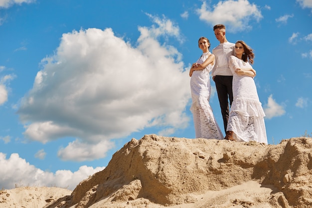 A guy and two girls pose on a sandy hill against the sky