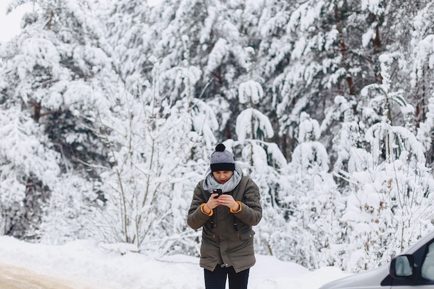 A guy walking along a snow-covered road near a pine forest with phone